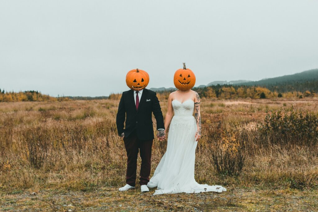 a bride and groom wearing pumpkin heads in a field