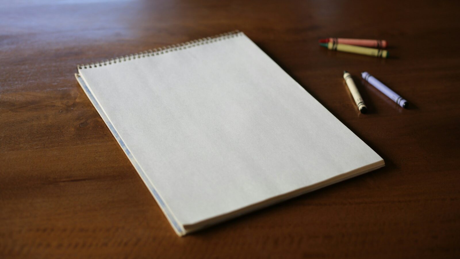 A notebook and some crayons on a wooden table