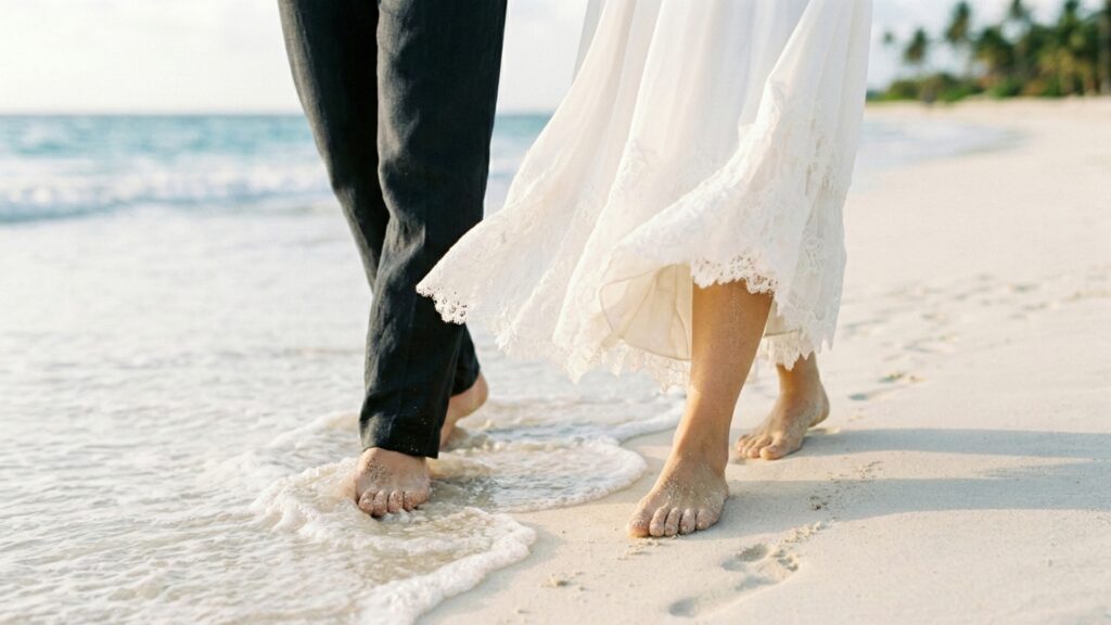 裸足で白い砂浜を歩く新郎新婦の足元